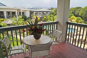A balcony with a table and chairs, overlooking a pool area with umbrellas and lounge chairs. - Club Wyndham Bali Hai Villas (Princeville)