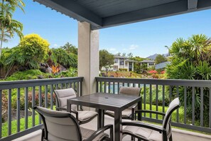 Un espace extérieur aménagé, abrité et doté de tables et de chaises, offrant une vue sur un jardin paysager et un plan d’eau.