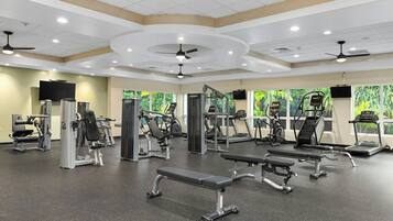 Un gimnasio con diversos equipos de ejercicio, como cintas de correr, máquinas de pesas y bancos.