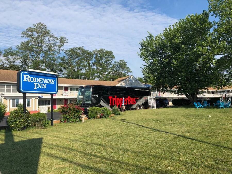 Un hôtel Rodeway Inn avec un grand autobus garé devant, entouré de verdure et d’arbres.