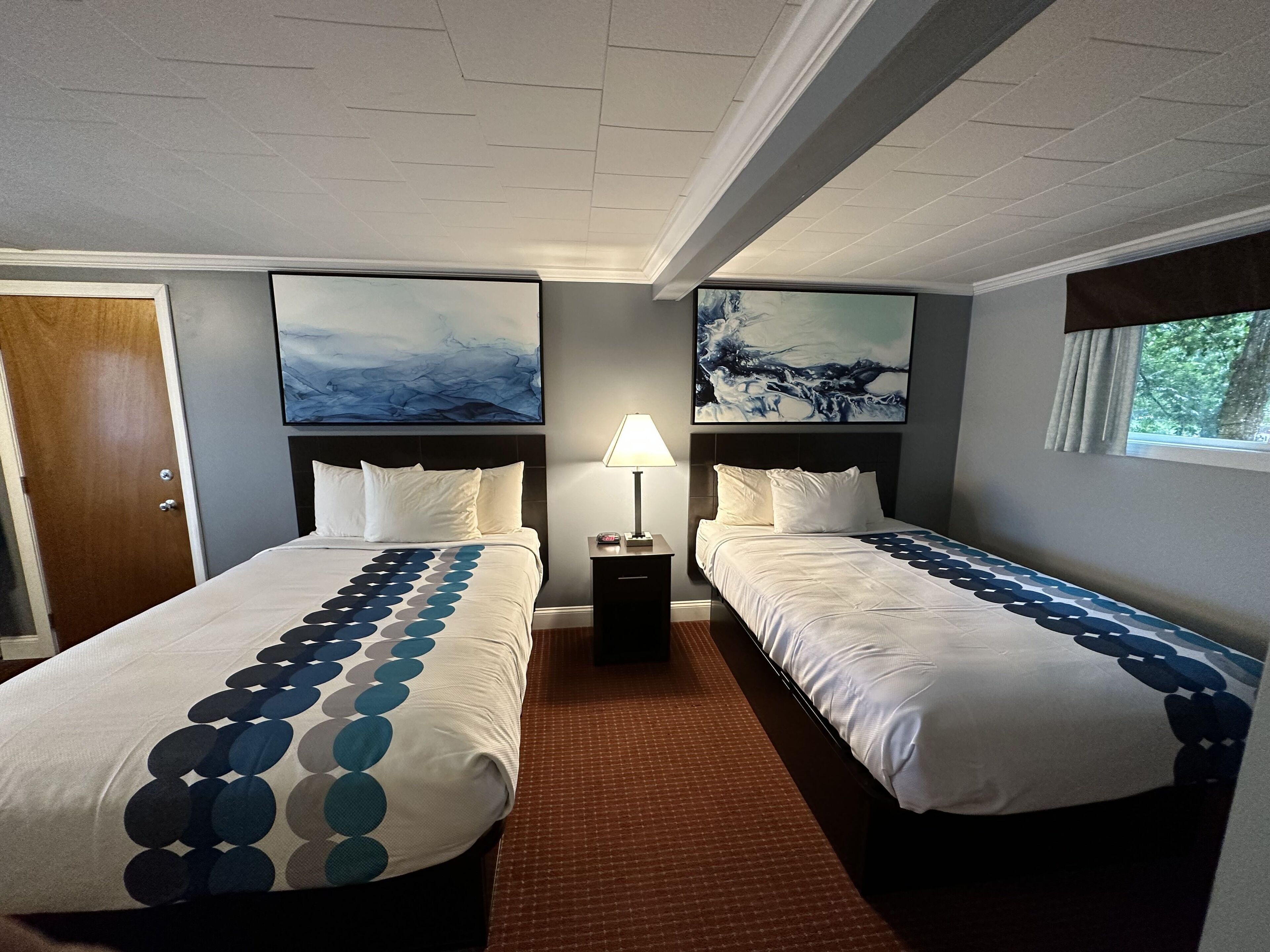 Una habitación de hotel con dos camas, una mesita de noche con lámpara y obras de arte en las paredes.