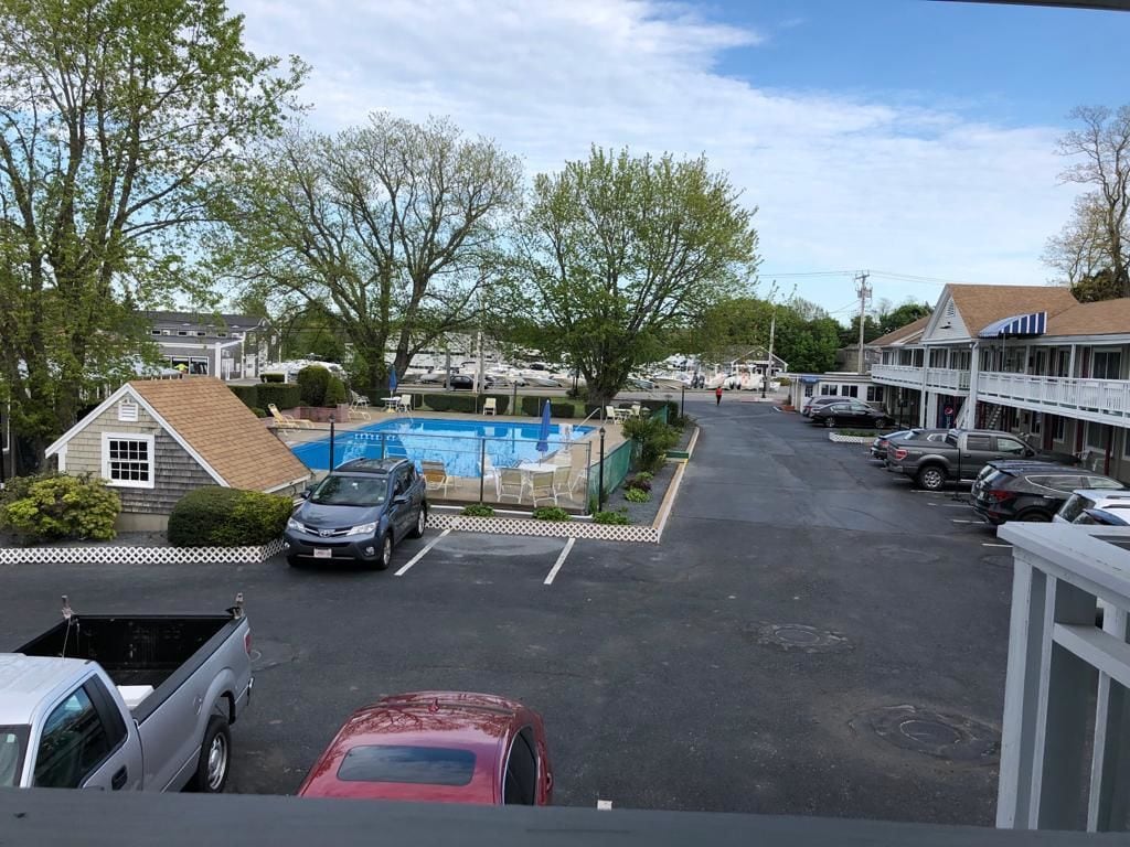 A parking lot with a swimming pool, a small building, and a row of cars.