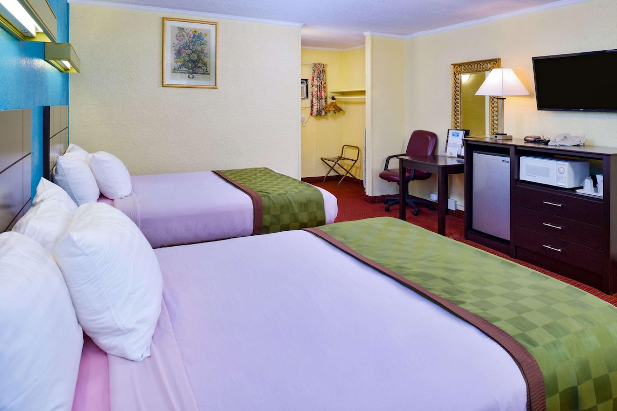 Una habitación de hotel con dos camas, un escritorio con computadora, televisor y microondas.