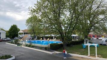 A residential area with a swimming pool, a large tree, and a person standing near the pool.