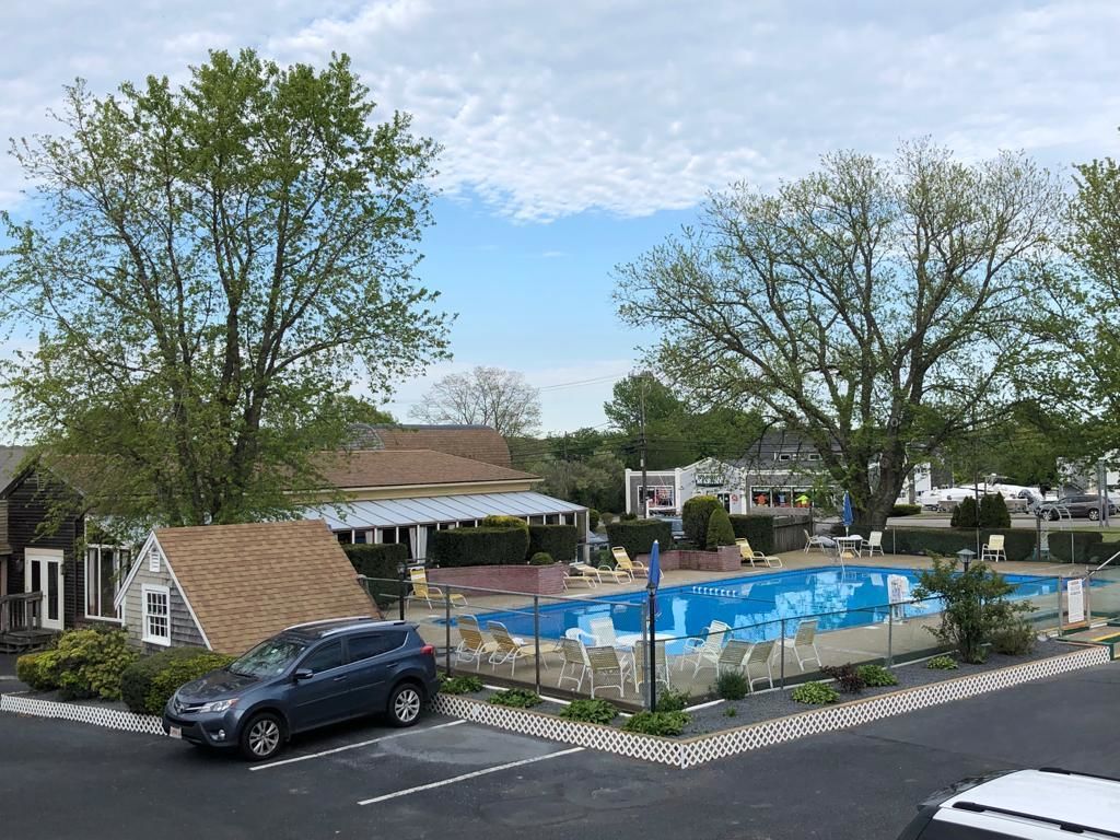 A swimming pool with lounge chairs, a parking lot, and a building with a sloped roof.