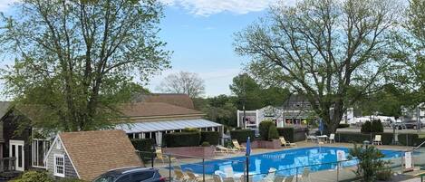 A swimming pool with lounge chairs, a parking lot, and a building with a sloped roof.