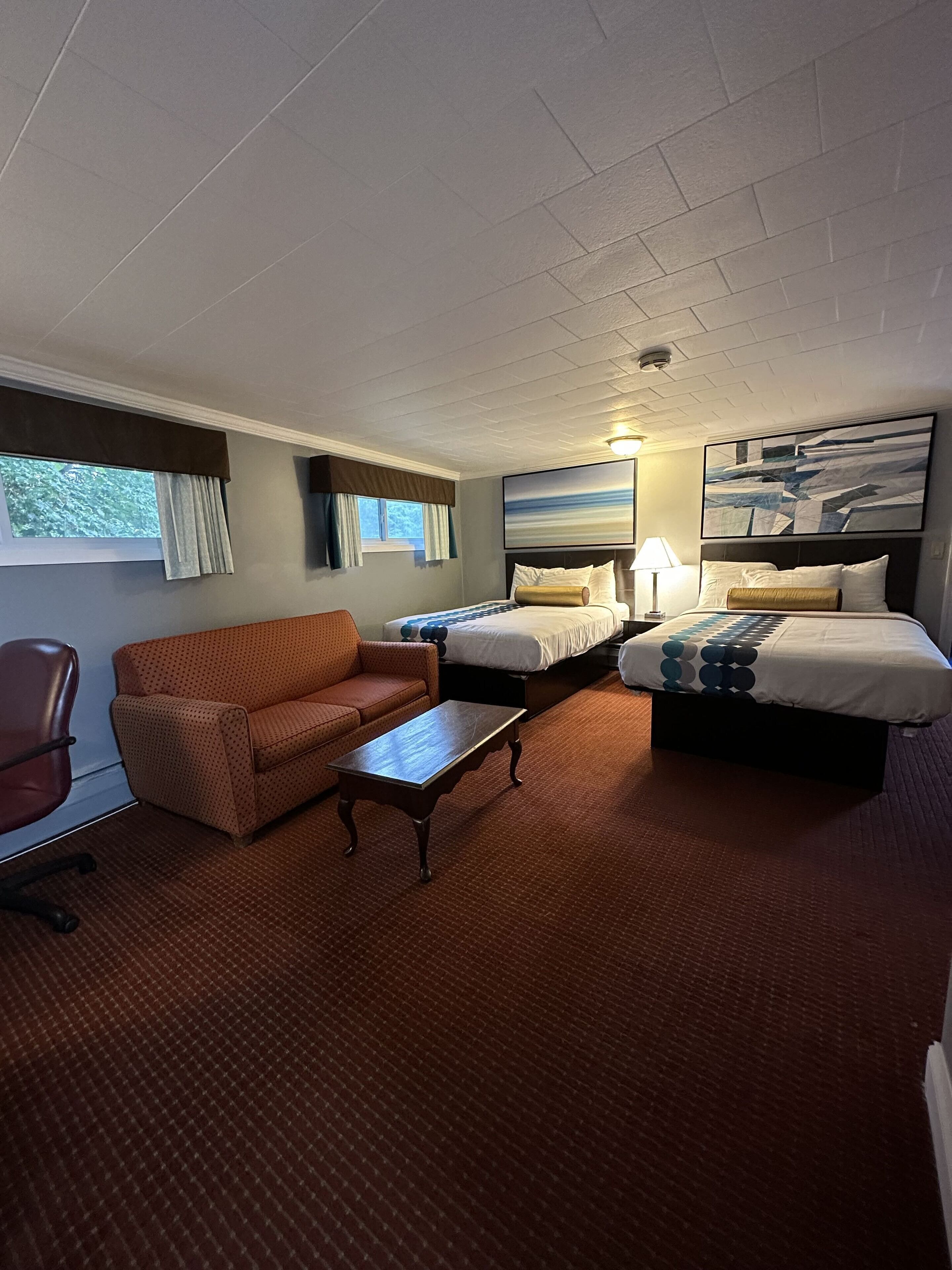A hotel room with two beds, a sofa, a chair, and a small table.