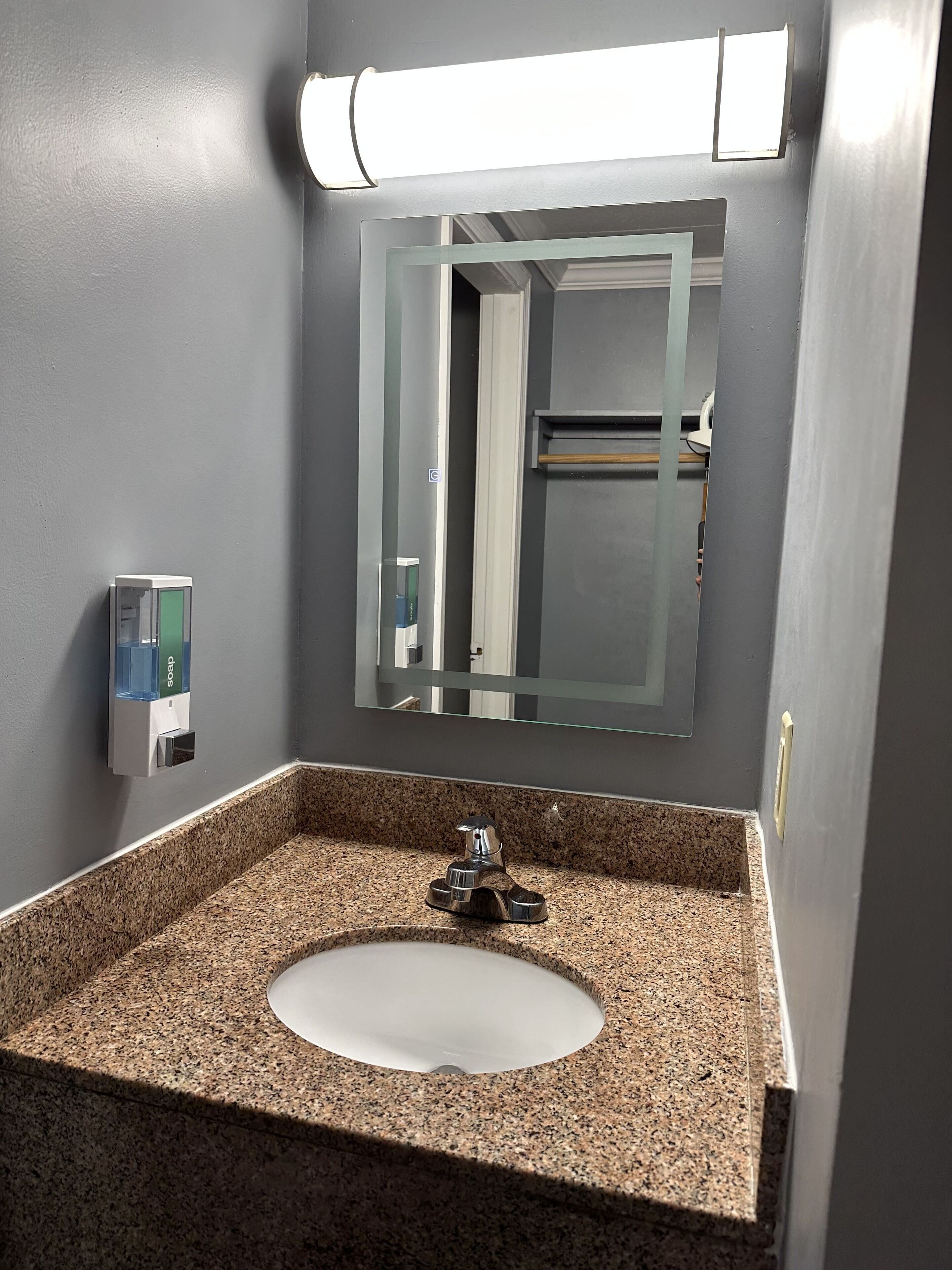 A bathroom with a granite countertop sink, a mirror, and a soap dispenser.