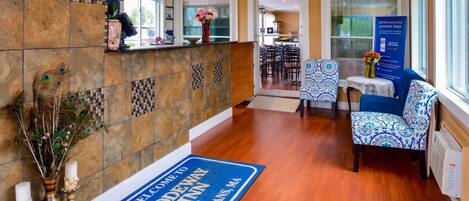 Un área de recepción con un tapete azul de bienvenida, un mostrador con un letrero 'Rodeway Inn' y sillones estampados.