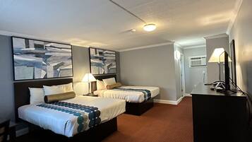 A hotel room with two beds, a desk, a lamp, and a television.