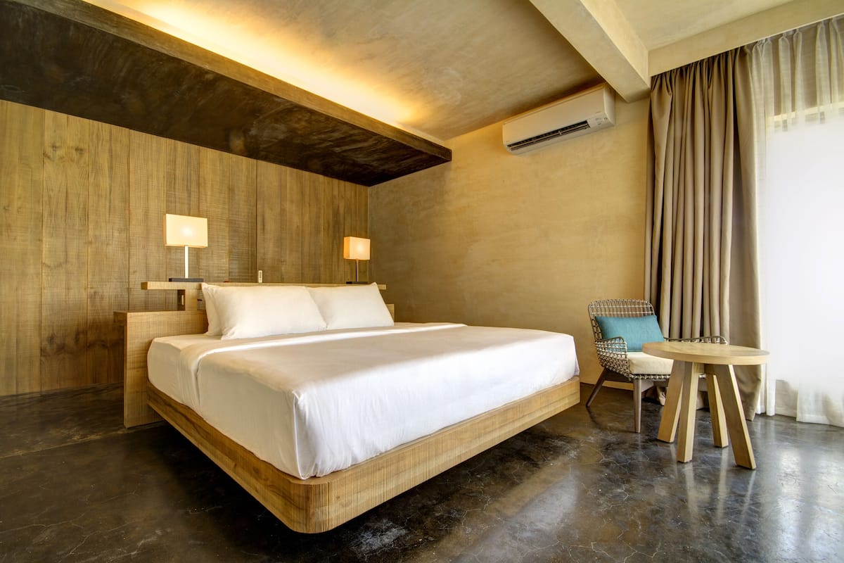 A modern hotel room with a wooden bed, two bedside lamps, a small round table, and a chair.