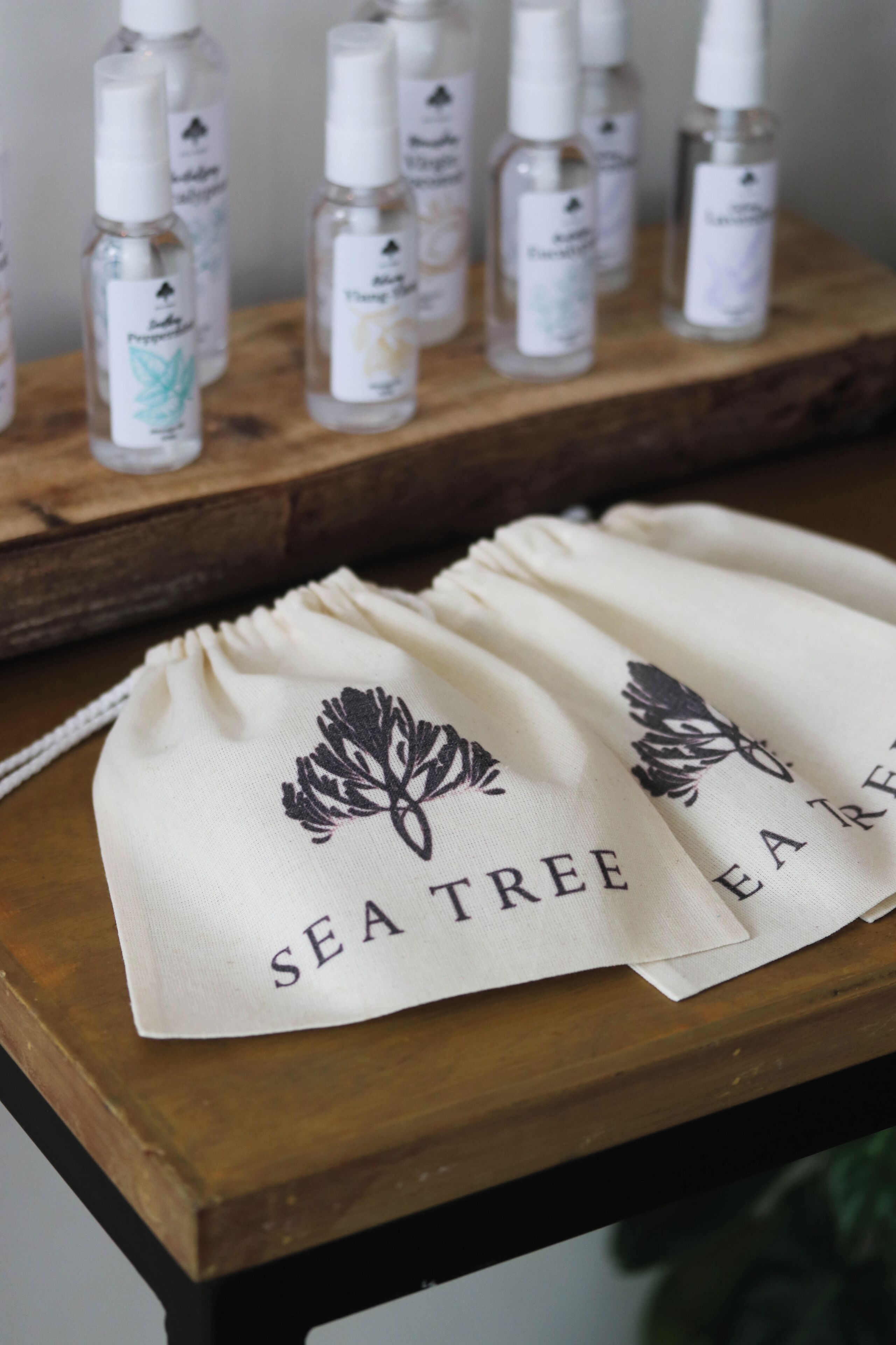 A wooden table with several bottles of skincare products and two drawstring bags with "SEA TREE" embroidered on them.