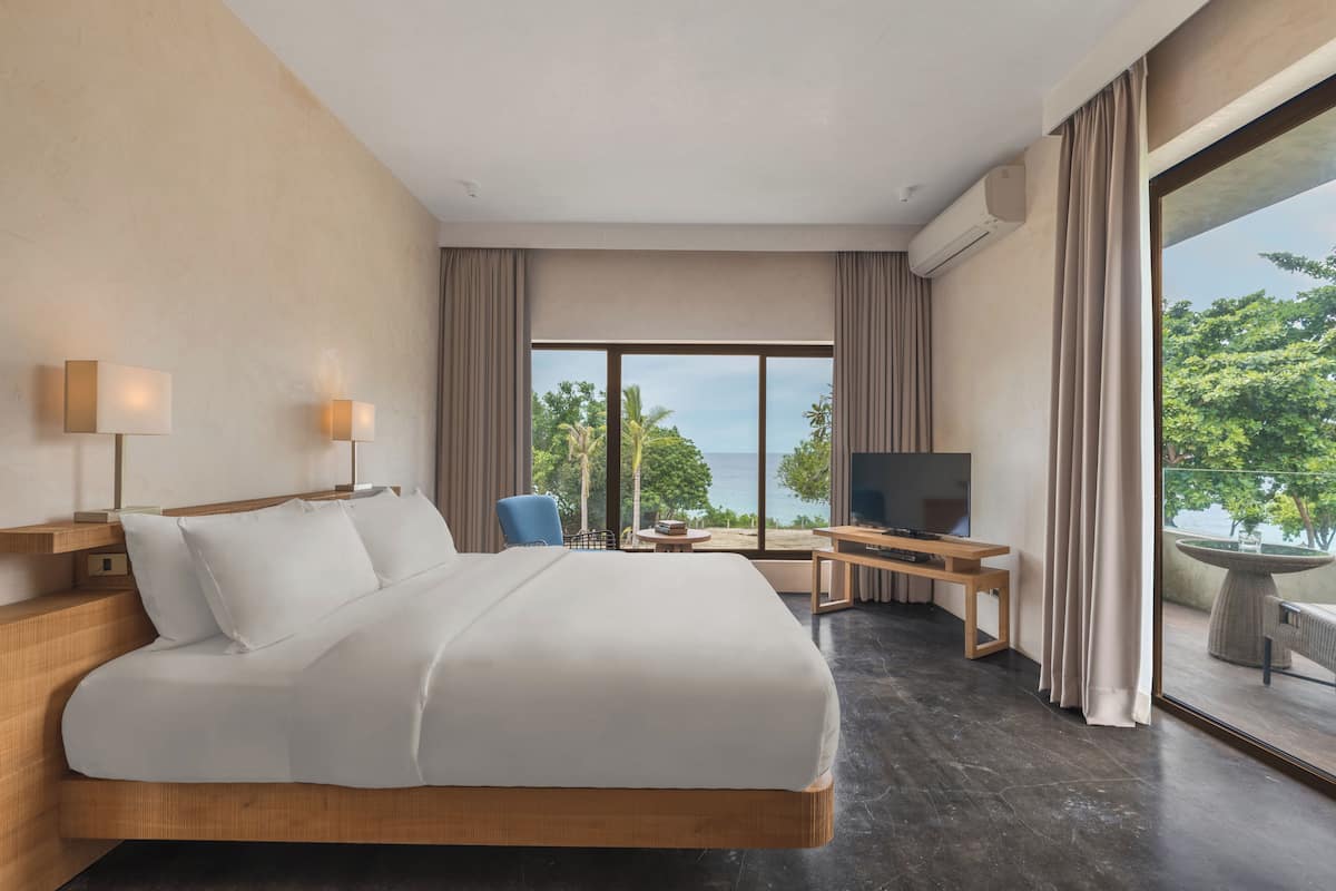 A hotel room with a large bed, a TV, a desk, and a view of the ocean.