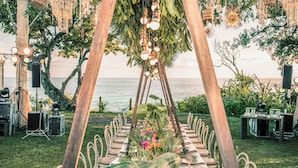 Un área de comedor al aire libre con una mesa larga preparada para recibir a los invitados, rodeada de vegetación y con vistas al océano.