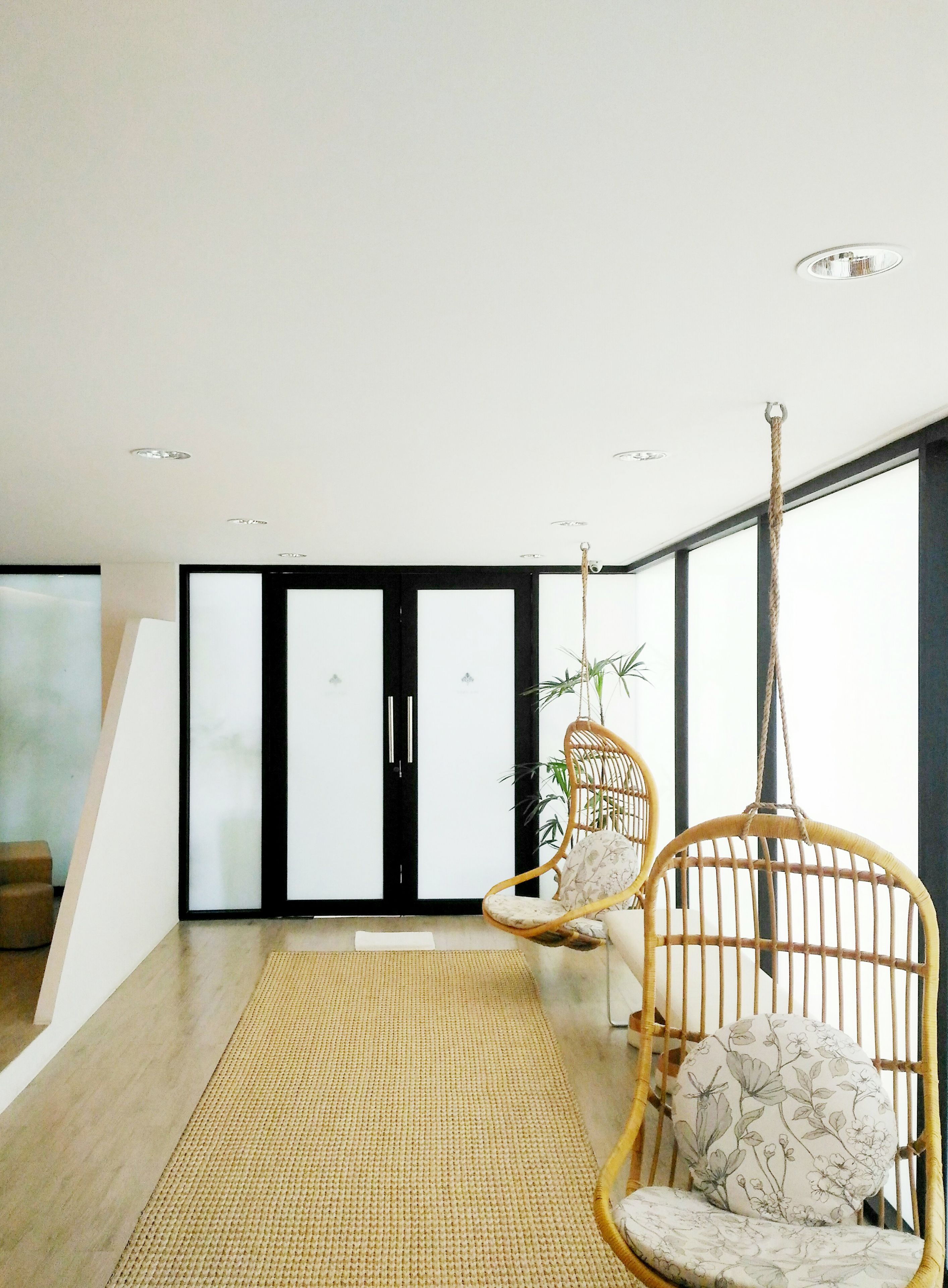 A modern interior with two wicker chairs, a woven mat, and a large window with a view.