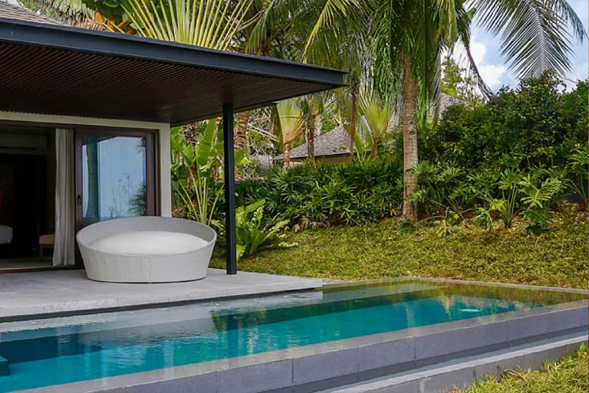 A modern outdoor pool area with a covered seating area, a dining table, and chairs.