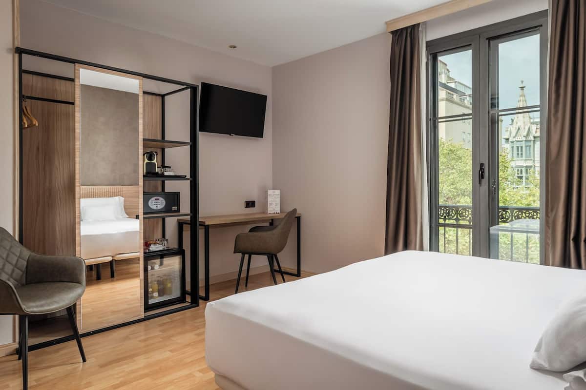 A hotel room with a bed, a desk, a chair, a TV, and a wardrobe.