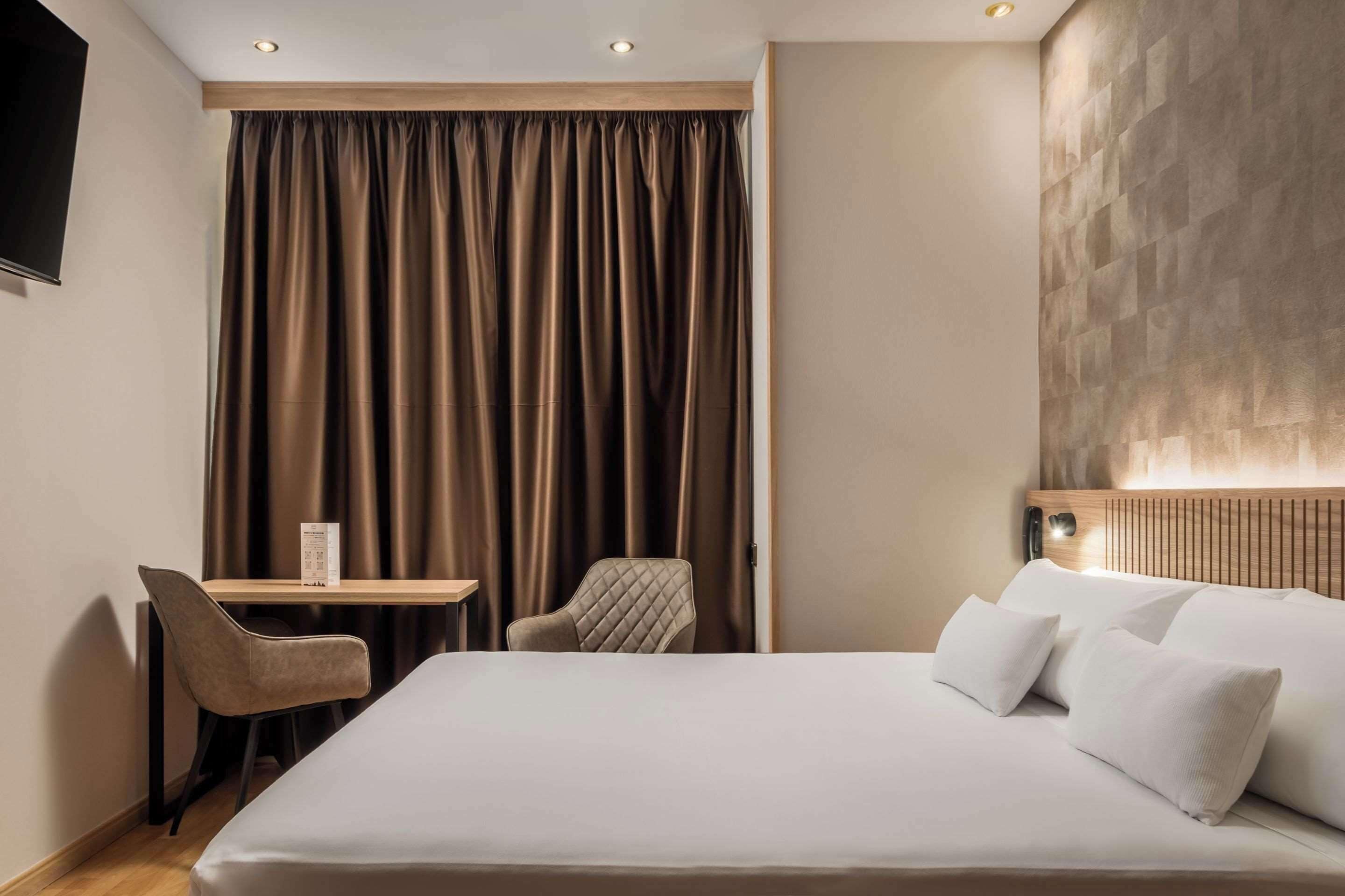 Una habitación de hotel con una cama grande, un escritorio con una silla, un televisor y una cortina.