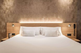 Camera d'albergo con testiera in legno, biancheria da letto bianca e telefono sul comodino.