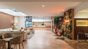 A spacious lobby with a reception desk, seating area, and a staircase with a floral wall. - Petit Palace Eixample (Barcelona)
