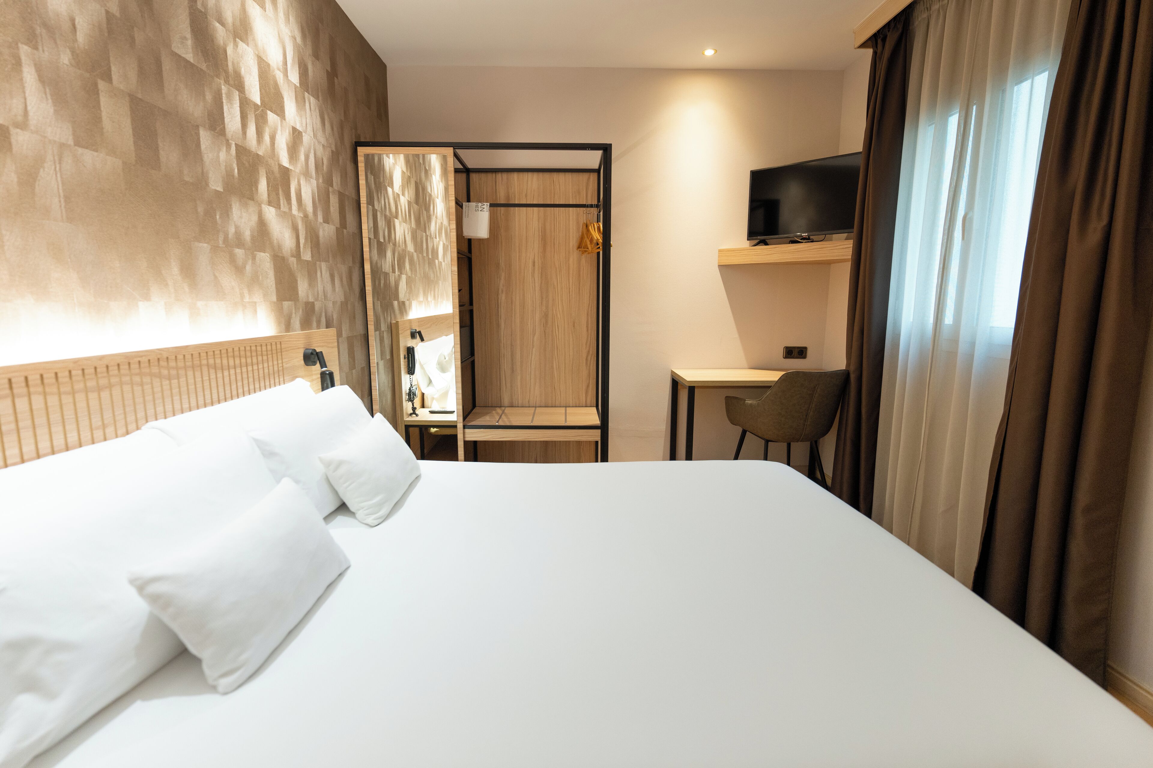 A hotel room with a large bed, a desk, a chair, a television, and a mirror.