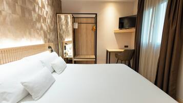 Una habitación de hotel con una cama grande, un escritorio, una silla, un televisor y un espejo.