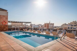 Una piscina sul tetto con sedie a sdraio e un galleggiante, circondata da edifici.