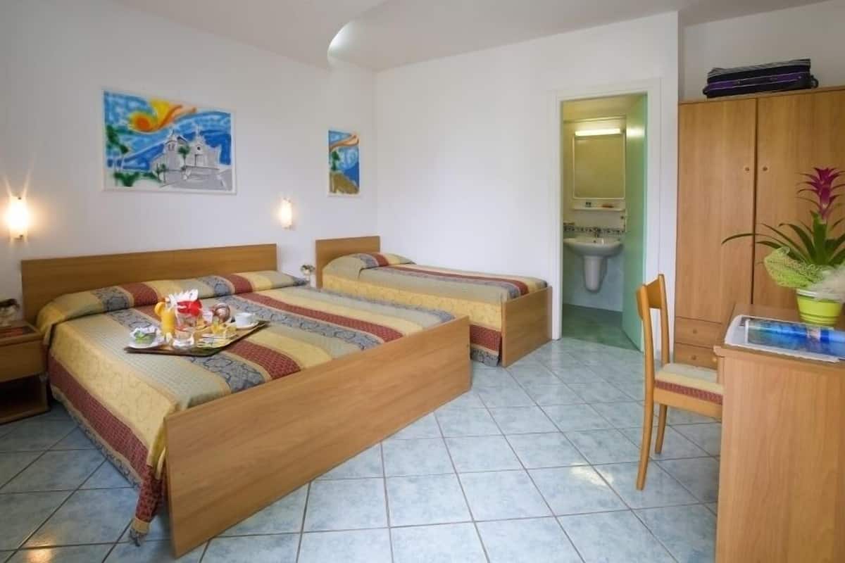 Habitación de hotel con dos camas individuales, un escritorio de madera, una silla, un lavabo y un armario.
