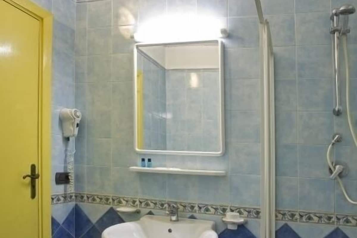 Un baño con puerta amarilla, un lavabo, un espejo y una ducha.