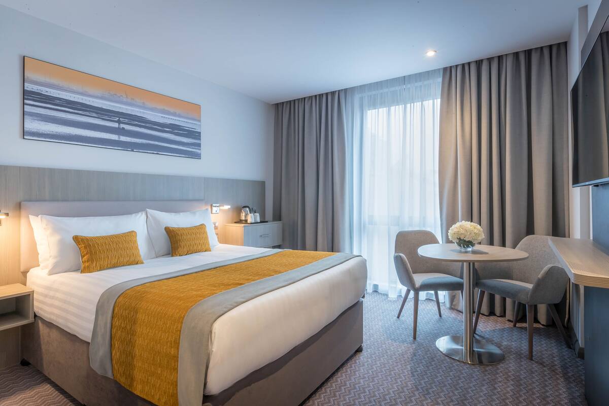 Habitación de hotel con una cama grande, un escritorio con dos sillas, una pequeña mesa con flores y un televisor en la pared.
