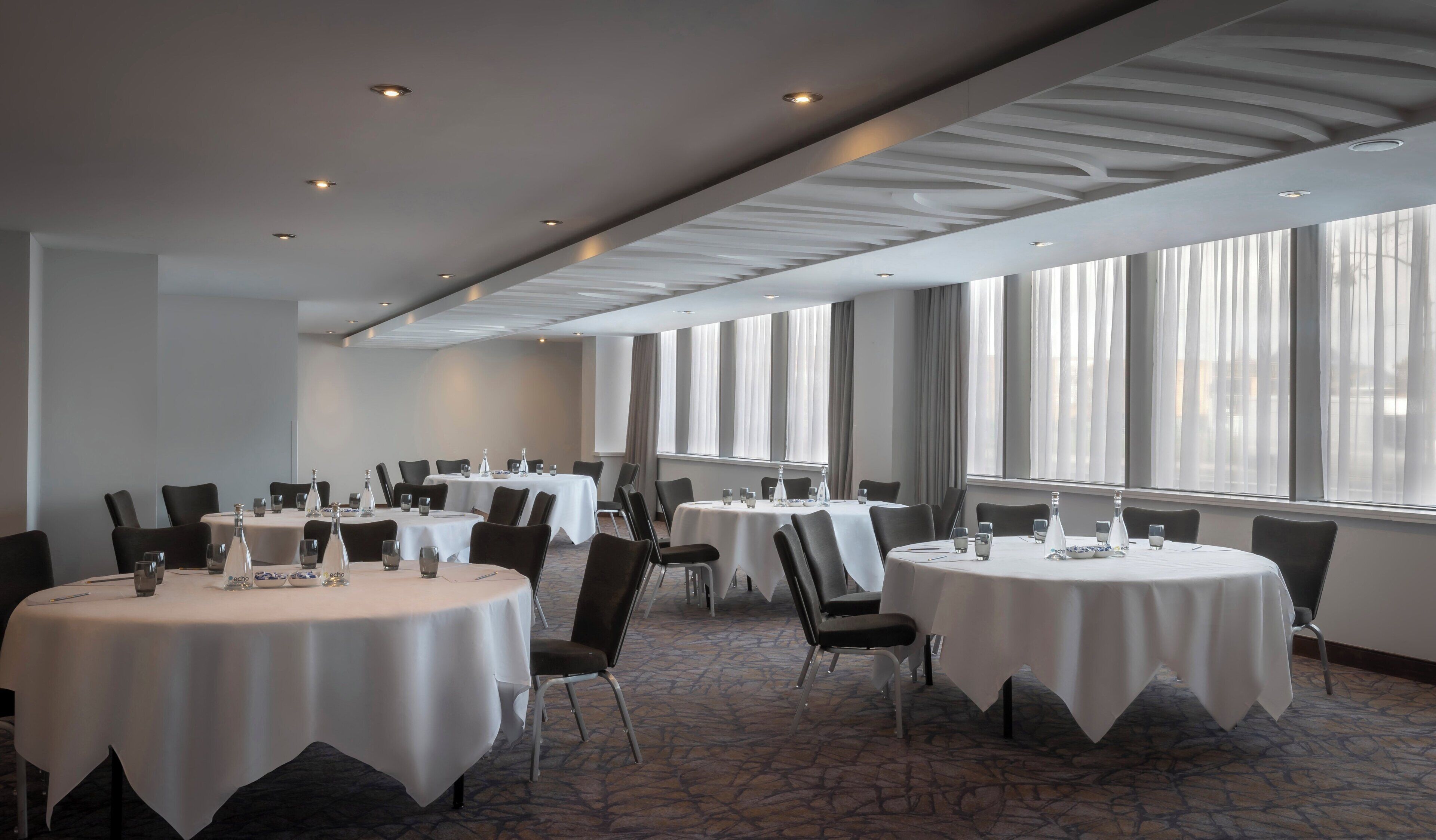 A conference room with round tables, chairs, and a large window with curtains.