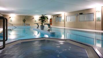 An indoor swimming pool with a hot tub, potted plants, and a clock on the wall.