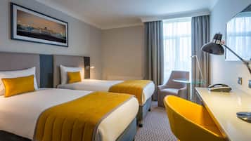 A hotel room with two beds, a desk, a chair, a lamp, and a window with curtains.