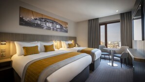Ein Hotelzimmer mit zwei Betten, einem Schreibtisch und Blick auf die Stadt.