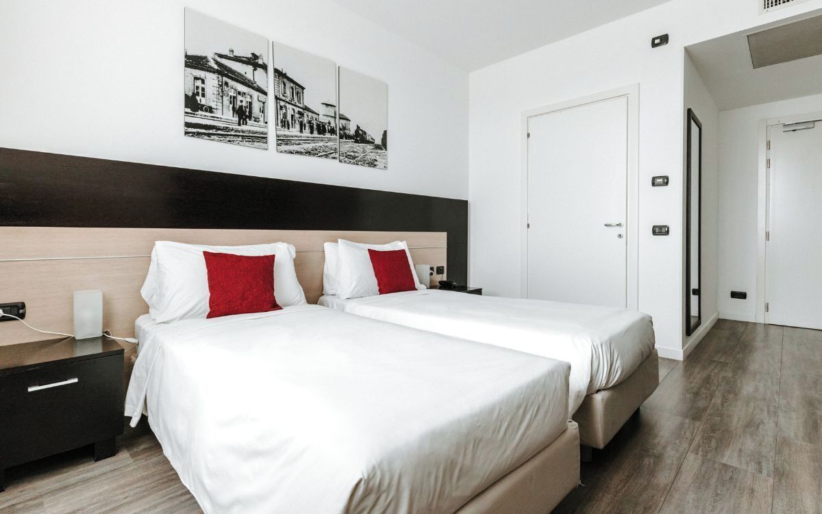 A modern hotel room with two beds, a wooden headboard, and a large window.