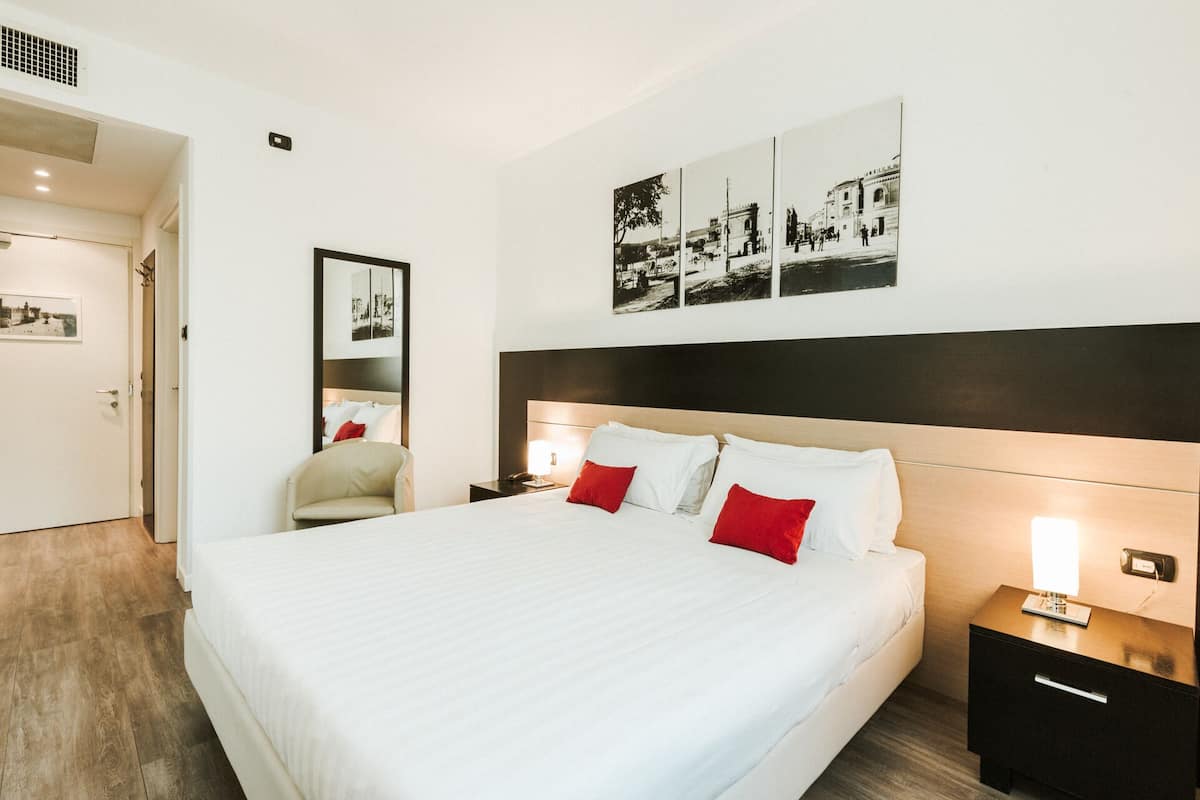 Une chambre d’hôtel avec un grand lit, une table de chevet avec une lampe, une chaise et une œuvre d’art accrochée au mur.