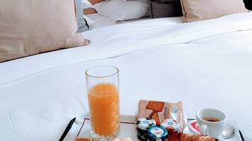 Ein ordentlich gedecktes Frühstücksbrett mit Croissants, einem Glas Orangensaft und verschiedenen Beilagen auf einem Bett mit einem hölzernen Kopfteil und Kissen.
