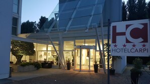 A hotel entrance with a glass facade, a sign reading "HOTELCARPI", and a paved area with potted plants. - Hotel Carpi (Carpi)
