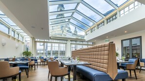 A modern dining area with high ceilings, a glass roof, and a view of a historic building.
