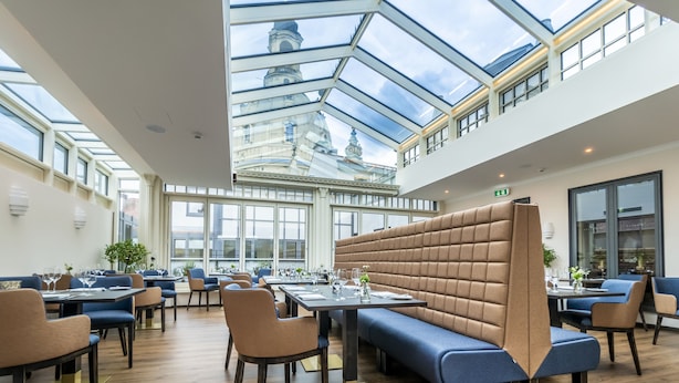 Un comedor moderno con techos altos, un techo de vidrio y vistas a un edificio histórico.