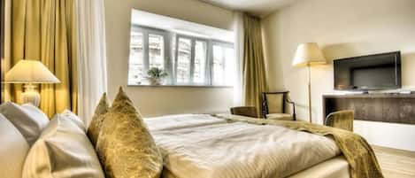 A hotel room with a large bed, two bedside lamps, a television, and a window with curtains.