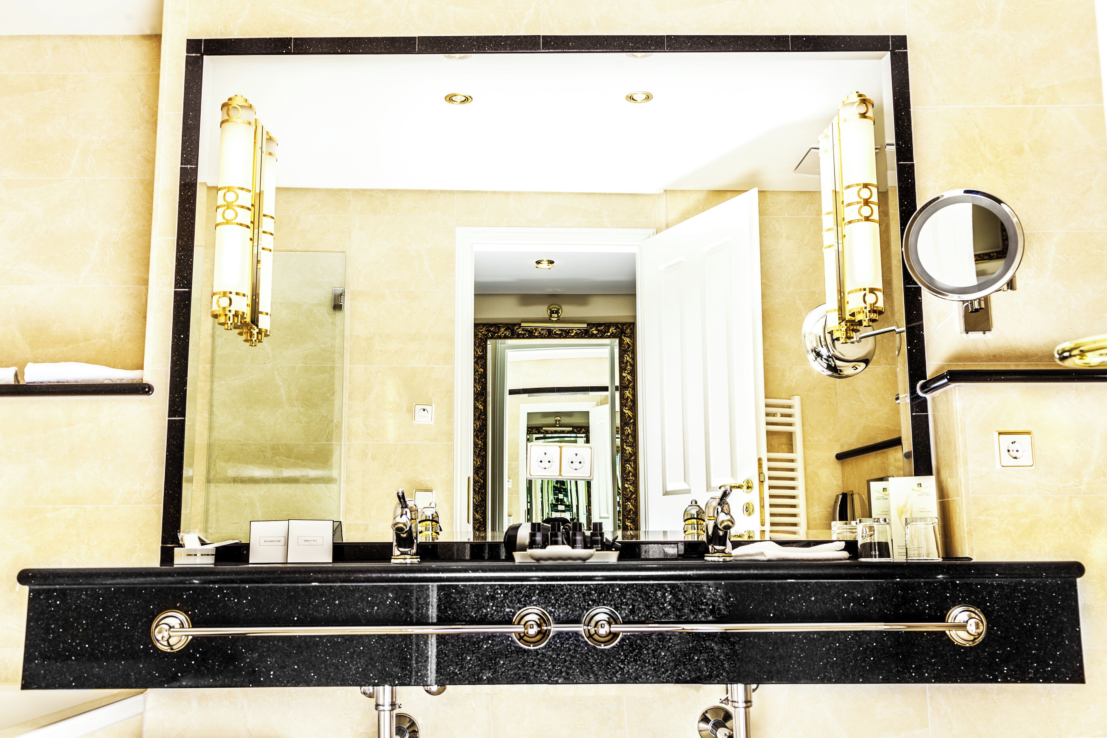 A bathroom with a large mirror, black countertop, and gold fixtures.