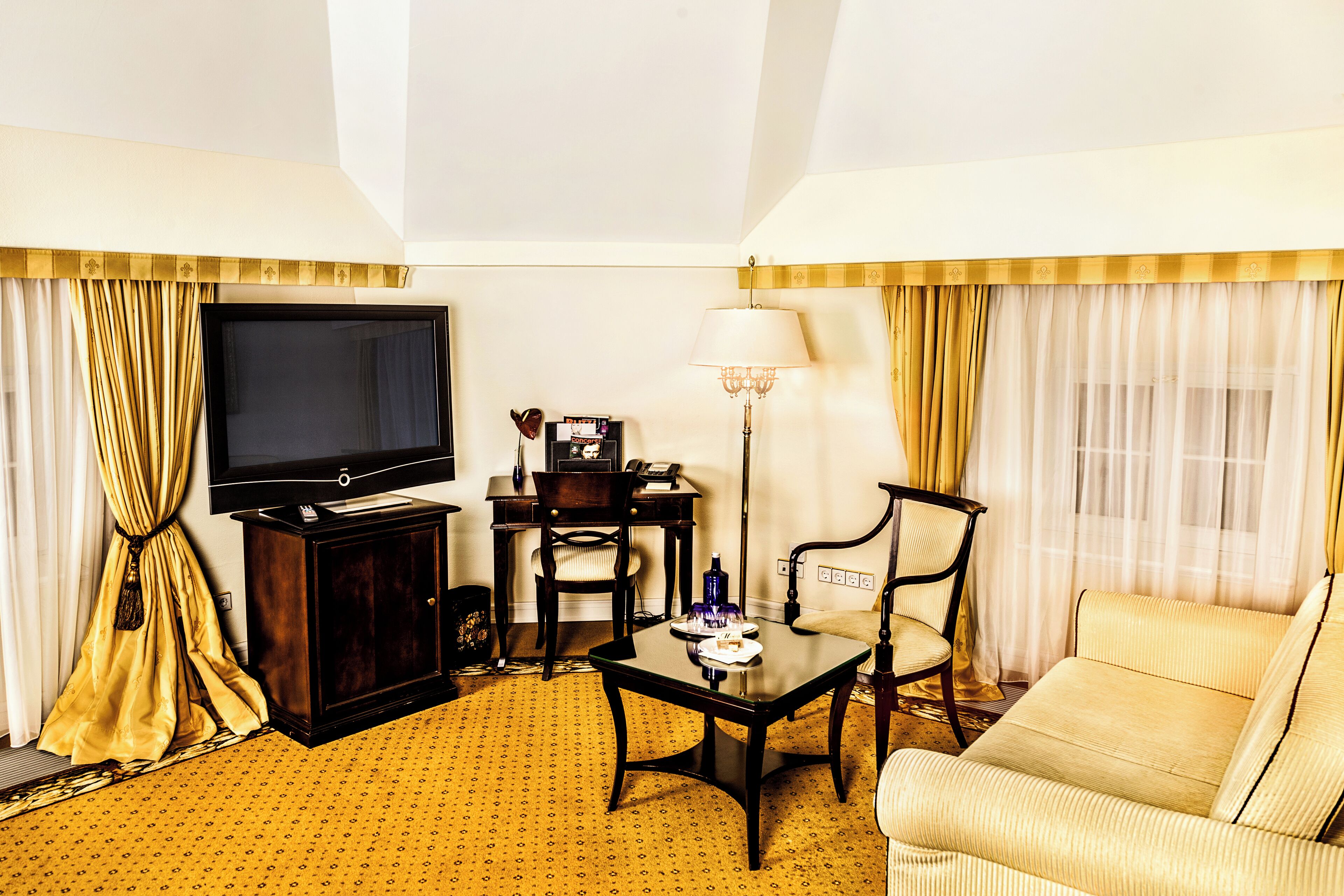 Habitación de hotel con televisión, escritorio, lámpara, sofá y cortinas.