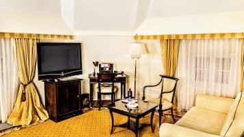 Habitación de hotel con televisión, escritorio, lámpara, sofá y cortinas.