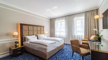 Ein Hotelzimmer mit einem großen Bett, einem Schreibtisch und einem Stuhl. Ein Nachttisch mit einer Lampe und einer Topfpflanze steht dort.