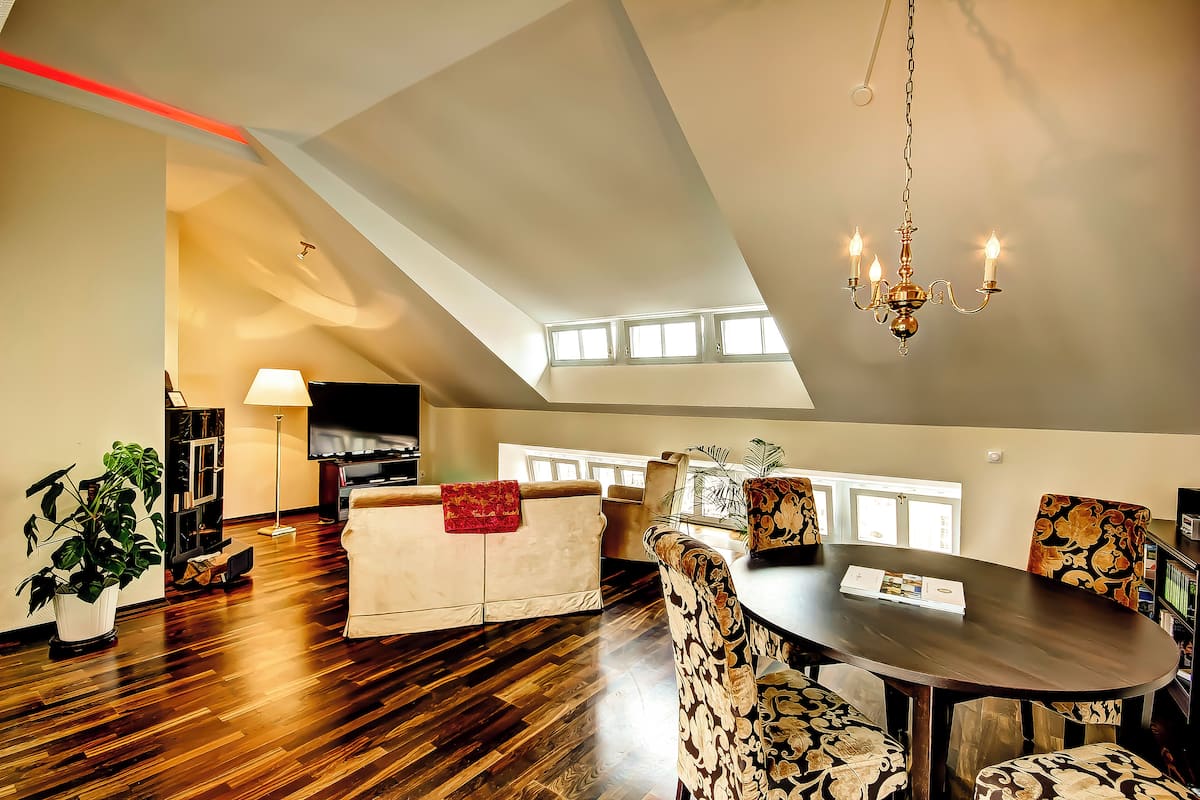 A spacious living room with a high ceiling, a chandelier, a dining table, and patterned chairs.