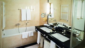 A bathroom with a bathtub, two sinks, a mirror, and a towel rack.