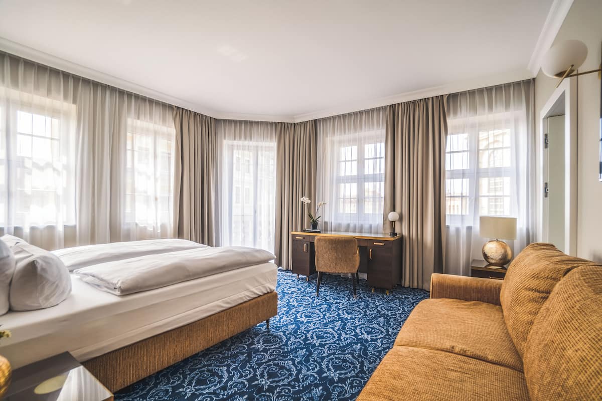 A hotel room with a bed, a desk, a sofa, and a patterned carpet.