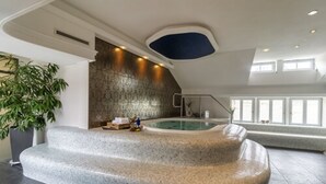 Un área interior de piscina moderna con un banco de piedra, una piscina pequeña y un ventanal que proporciona luz natural.