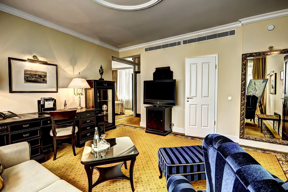 A hotel room with a sofa, a table, a lamp, a television, and a mirror.